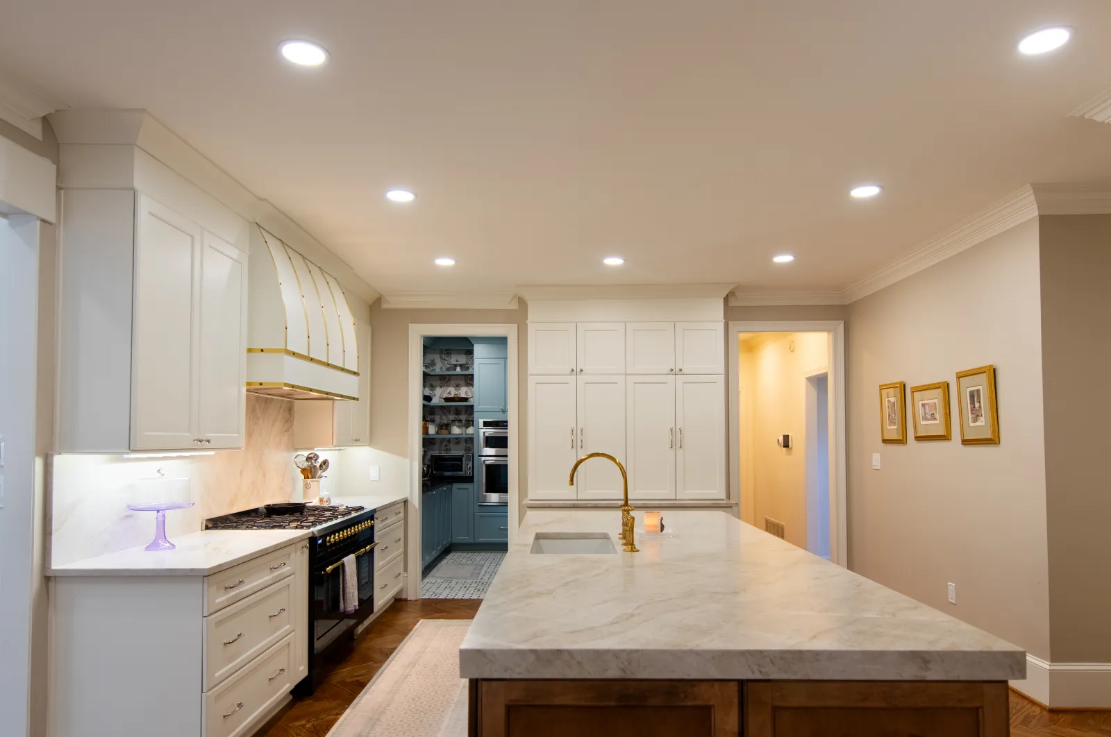 Modern kitchen with large marble island, brass faucet, white cabinetry, and recessed ceiling lights