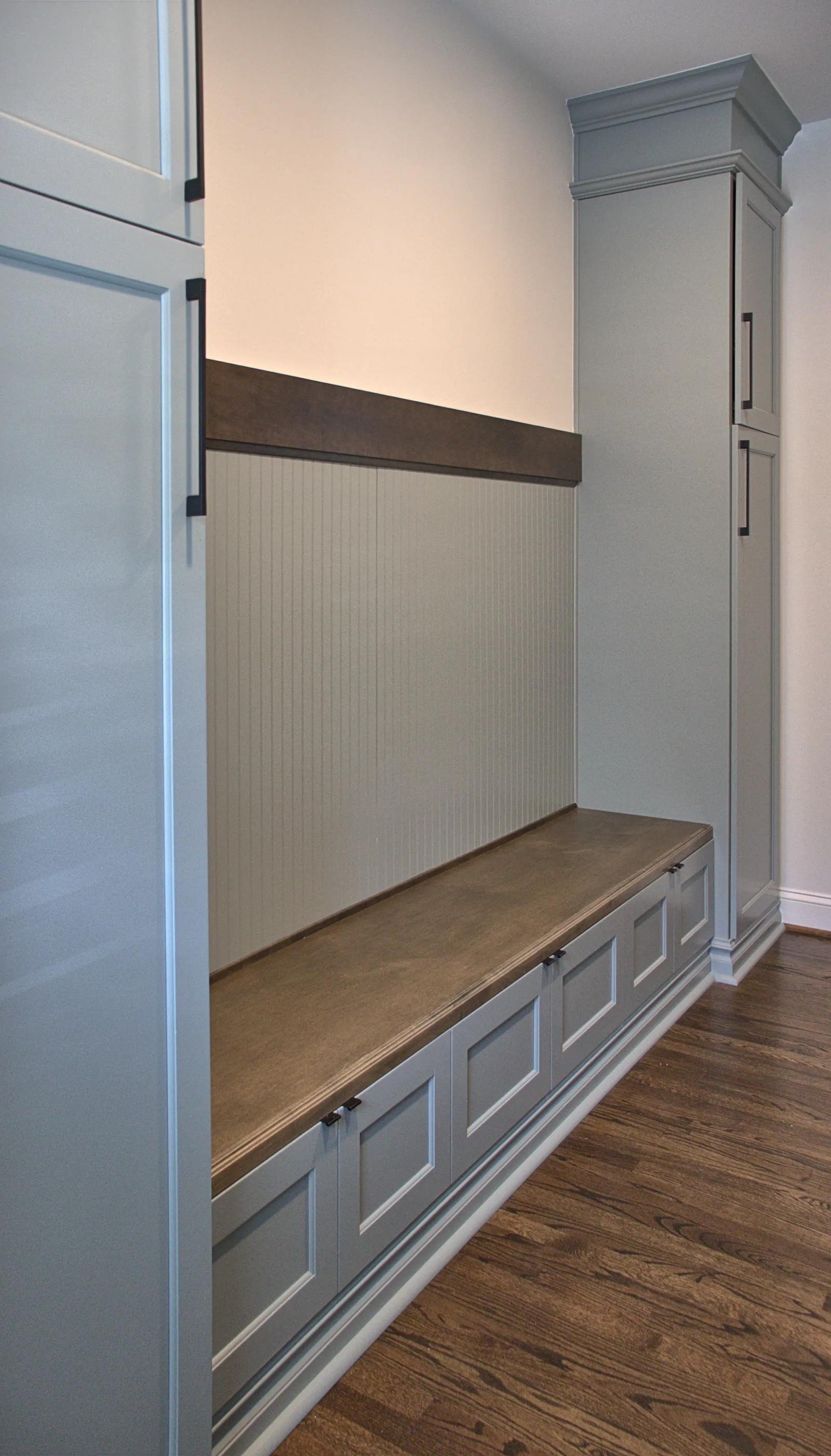 Built-in gray storage bench with wooden seat and tall cabinet in a room with hardwood floor.