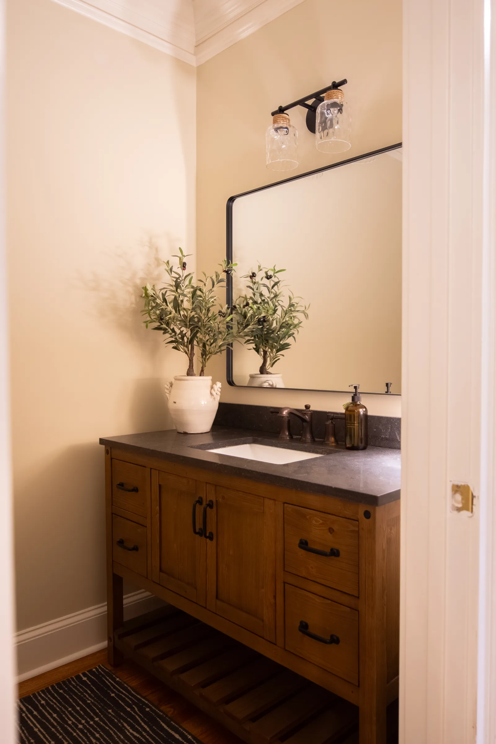Rustic wooden bathroom vanity with black countertop, rectangular mirror, light fixture, and potted plant