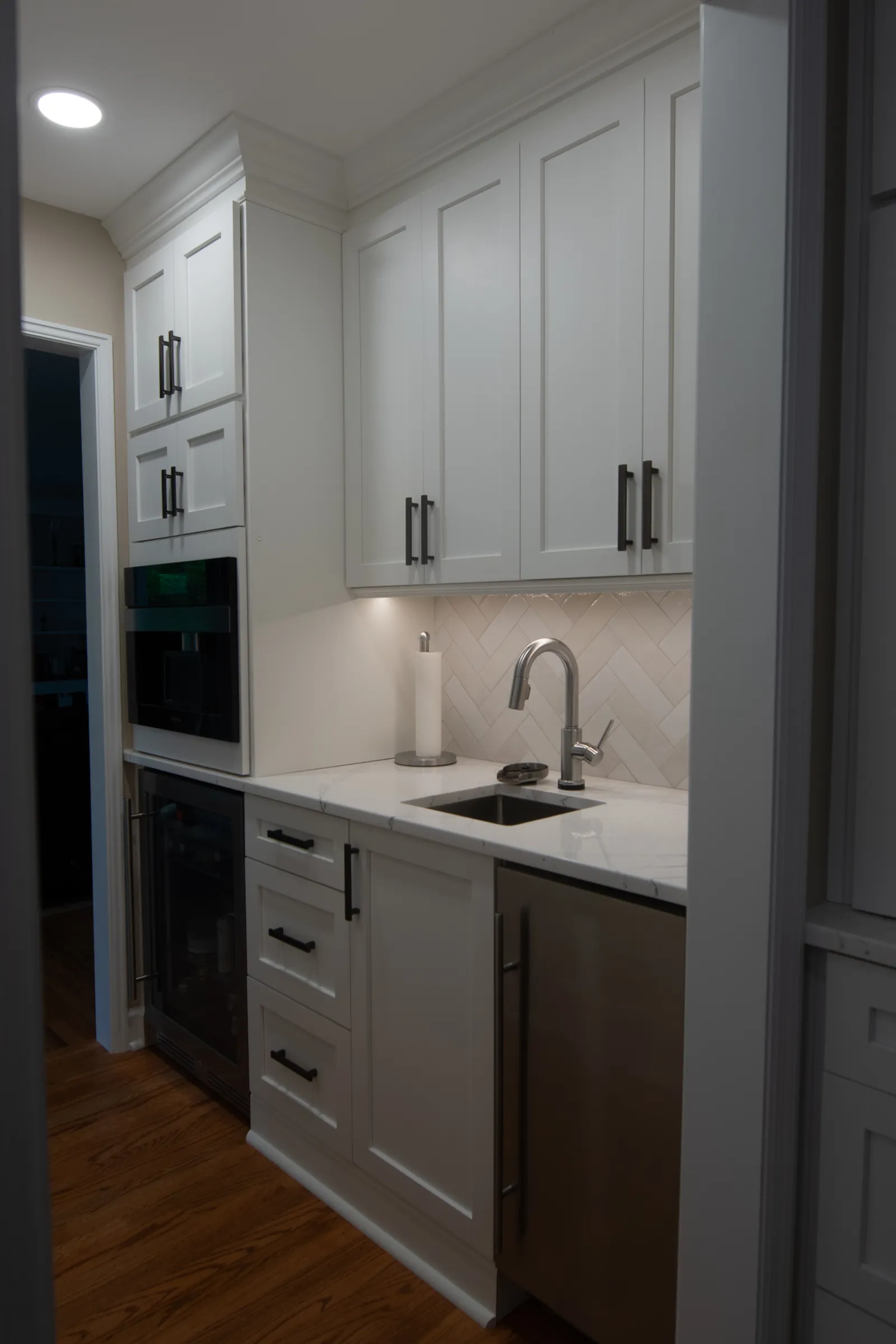 Modern kitchen with white cabinets, stainless steel sink, built-in appliances, and wooden floor.