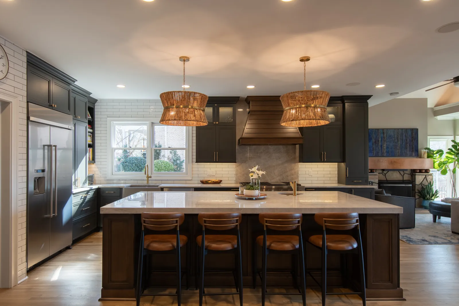 Modern kitchen with large marble island, dark cabinets, wicker pendant lights, and stainless steel appliances.