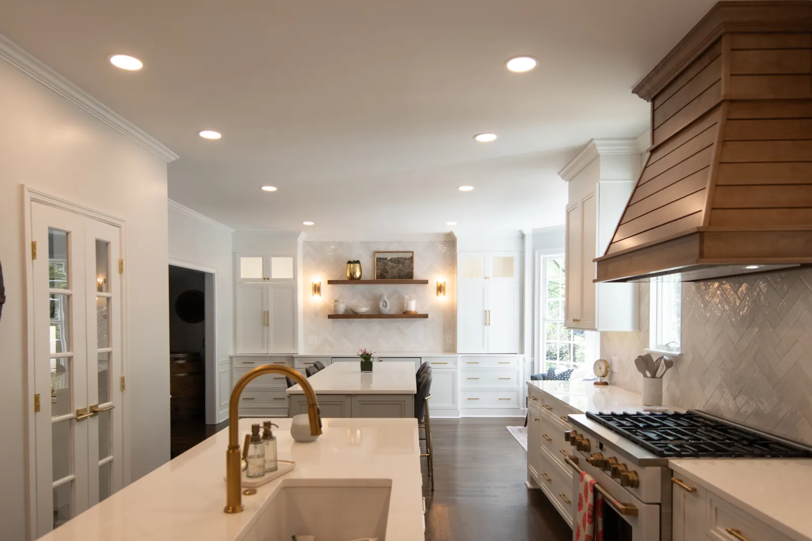 Modern kitchen with white cabinets, gold fixtures, wood range hood, and central island with marble countertop.
