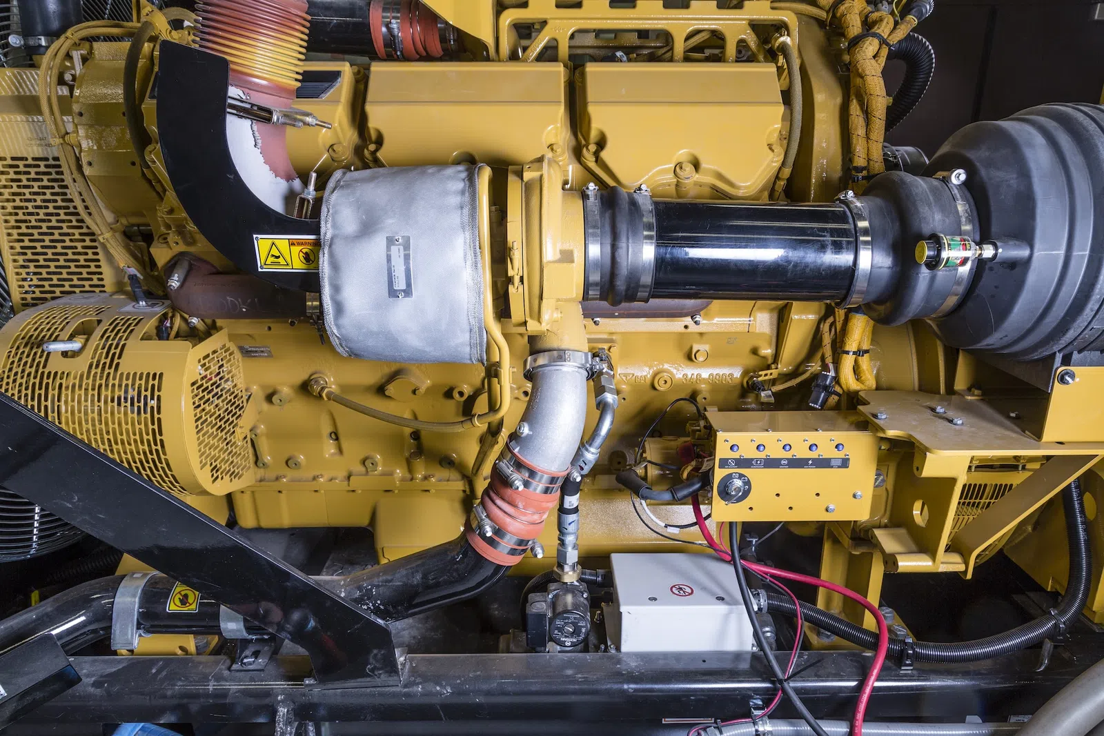 Close-up of a large industrial yellow diesel engine with pipes, wires, and control panel components.