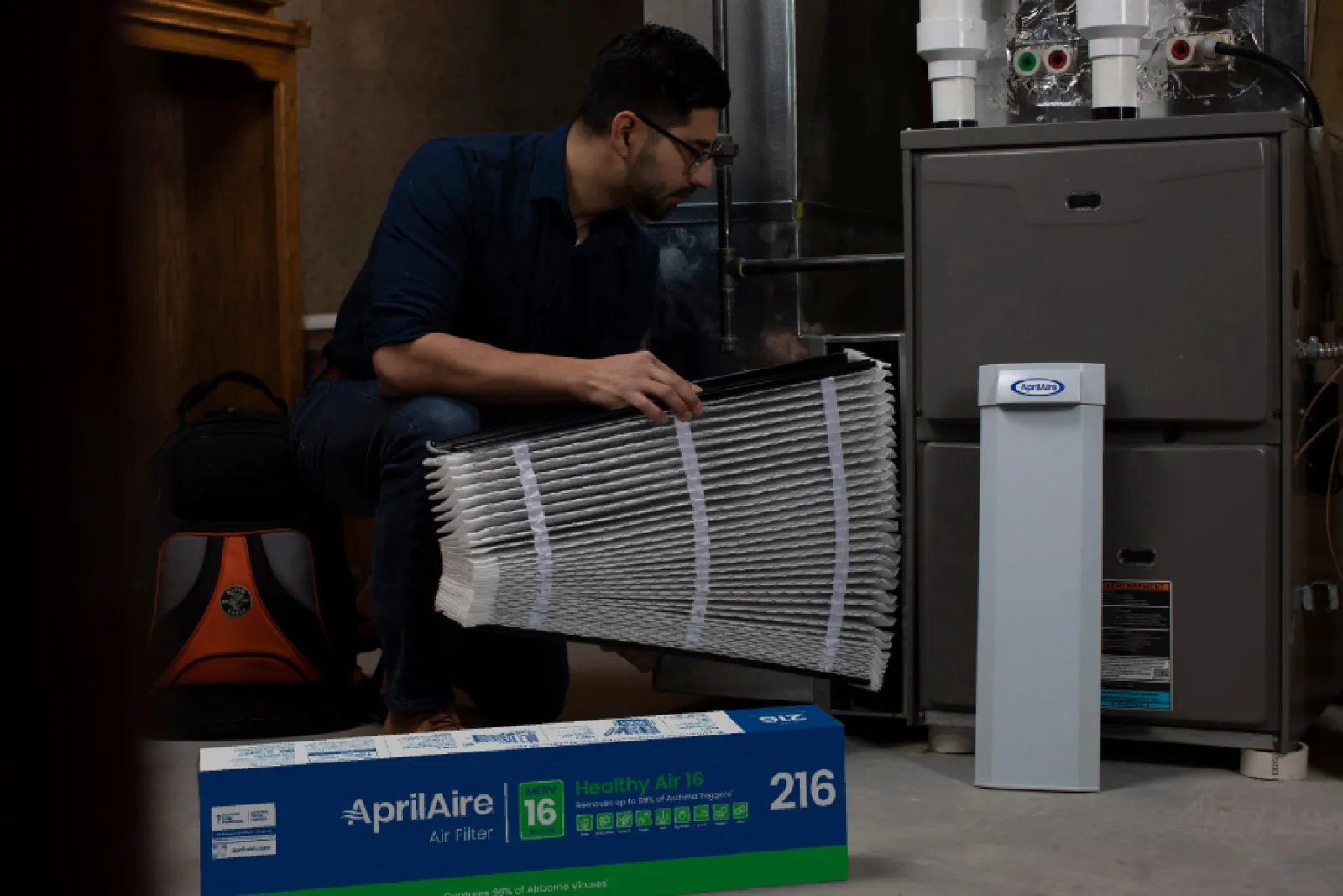 Technician installing an AprilAire whole-house MERV 13 air filter into a media filter cabinet next to a furnace