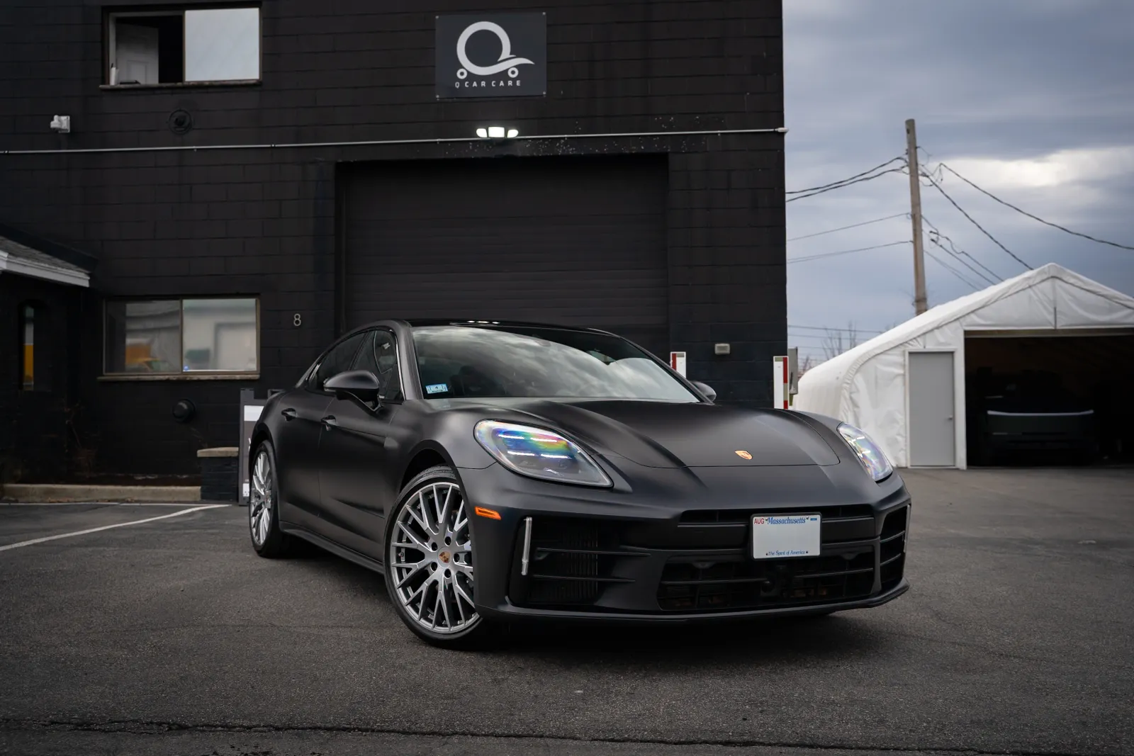 Matte black luxury Porsche sports car parked outside a modern black building under cloudy sky.