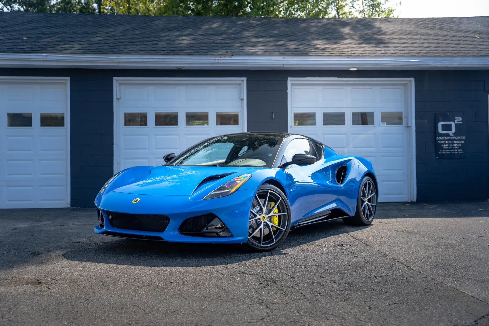 Blue sports car parked in front of three white garage doors on a sunny day