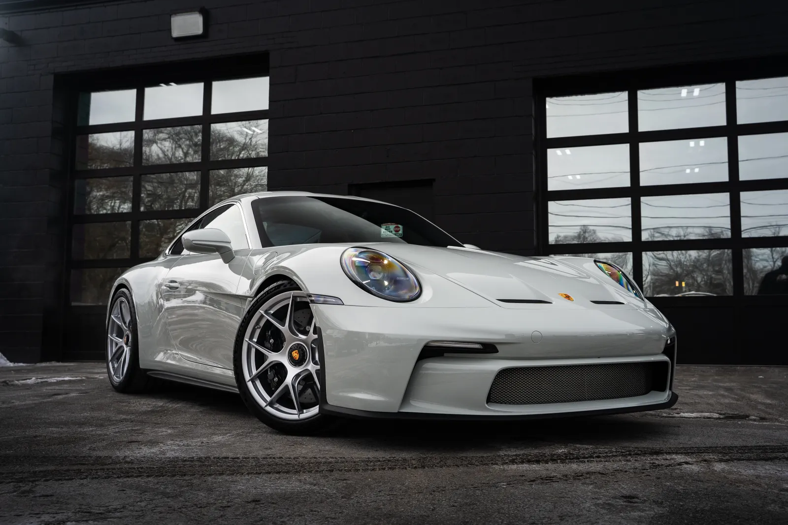White Porsche sports car parked in front of a black garage with large glass windows.