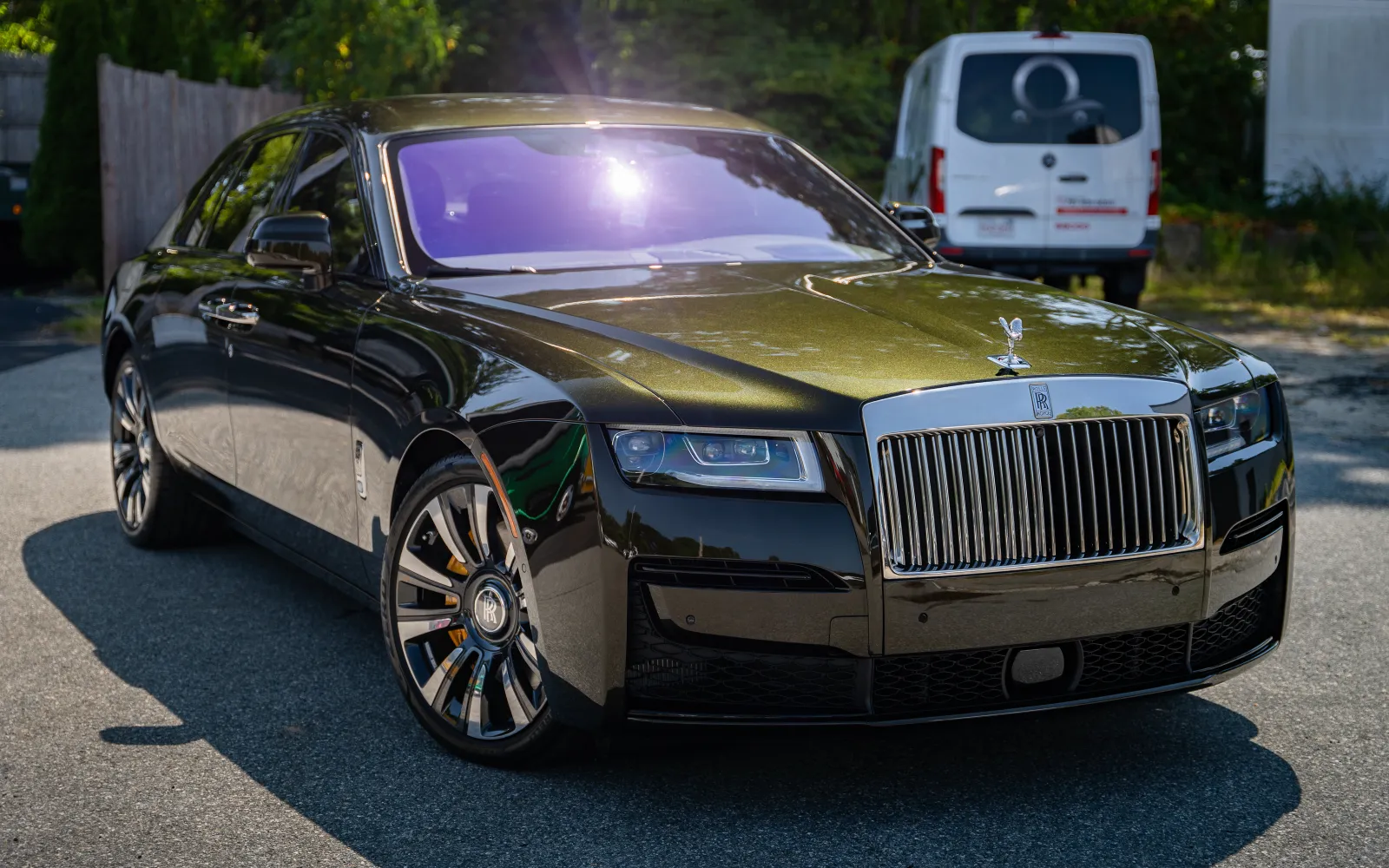 Shiny black Rolls-Royce Phantom parked on a sunny street with reflections and luxury details visible