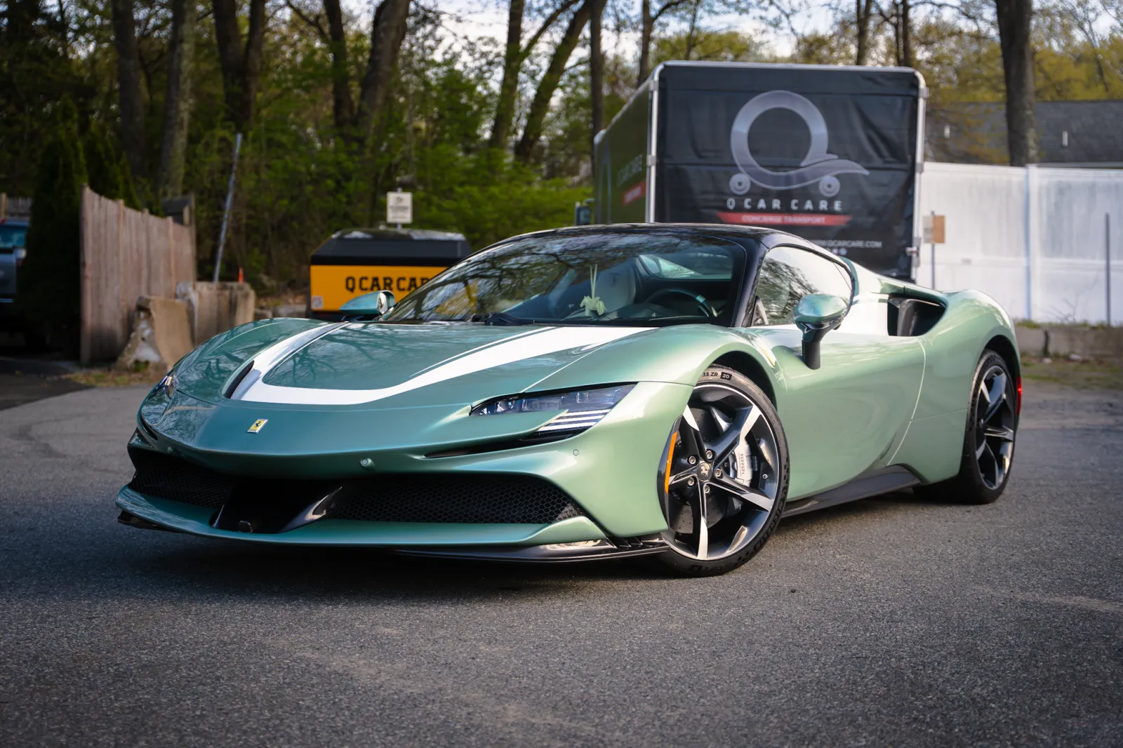 Green Ferrari SF90 Stradale sports car parked outdoors on asphalt near trees and fences.