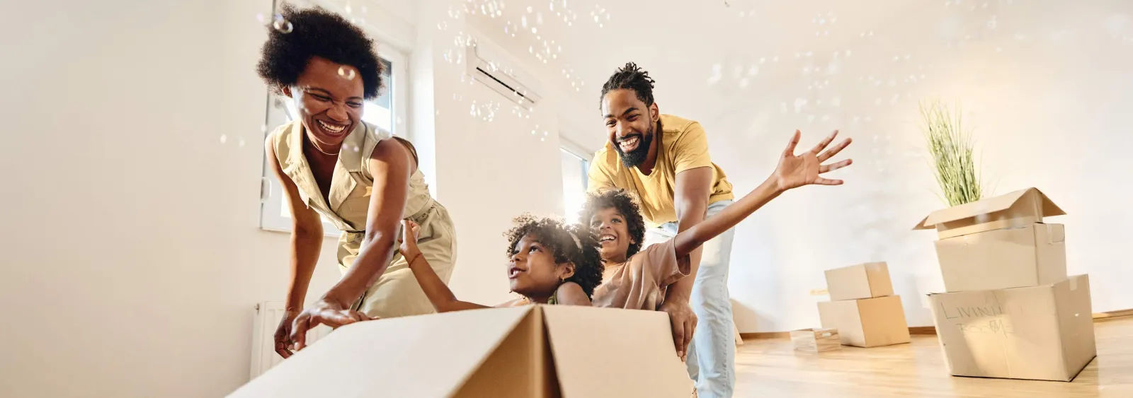Happy family playing with moving boxes in a bright, empty room during a house move.