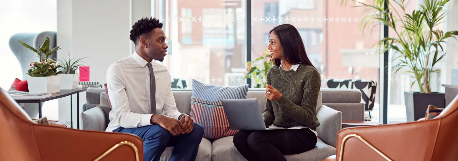 Man in shirt and tie and woman with laptop having a business chat in a modern office lounge area.