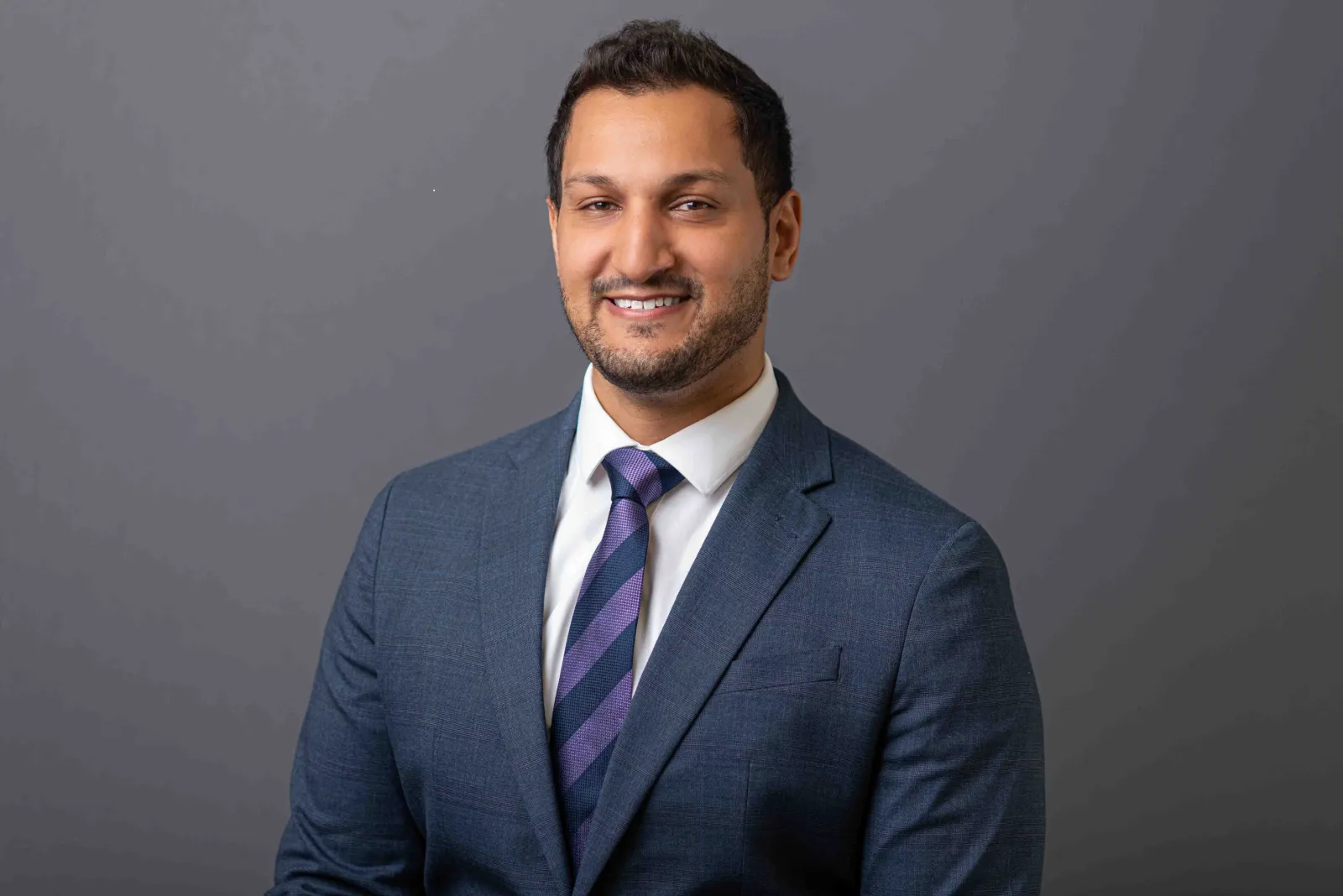 Dr. Usker Naqvi poses in front of a gray backdrop.