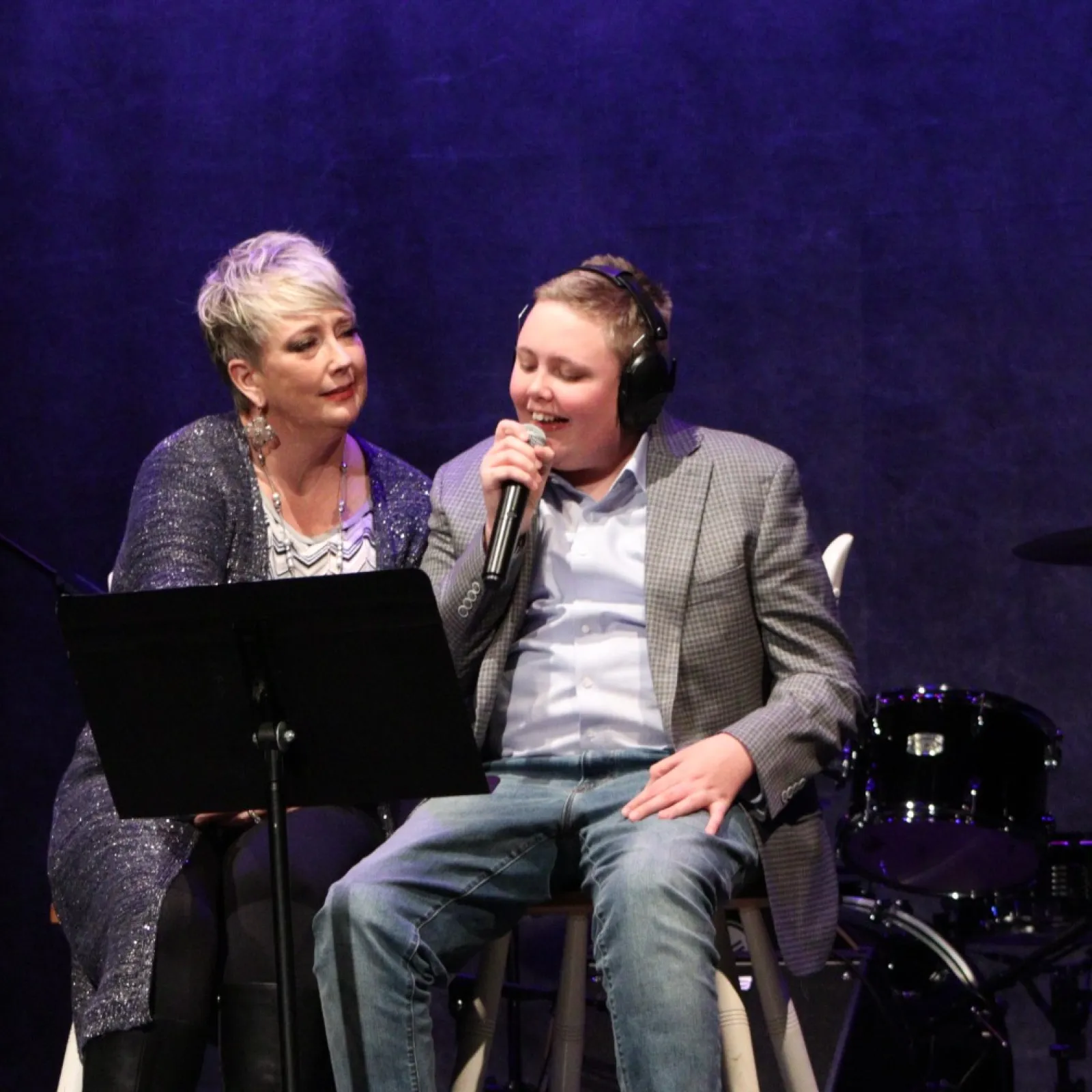 a man and woman sitting on stools with microphones and drums