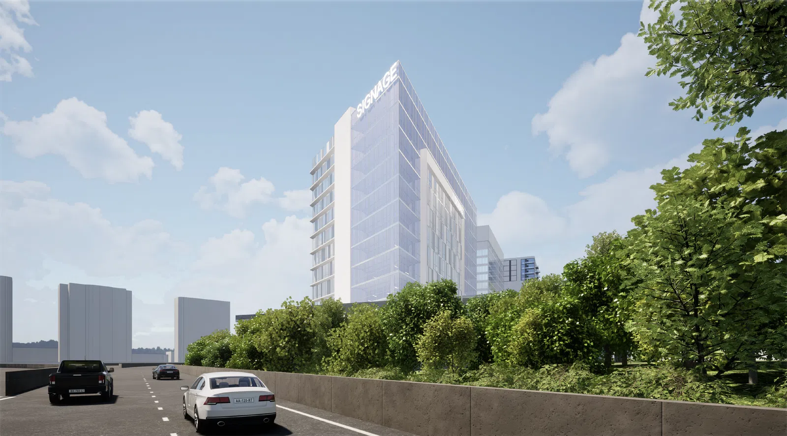 Modern glass office building with signage, surrounded by greenery alongside a busy street with cars under a blue sky.