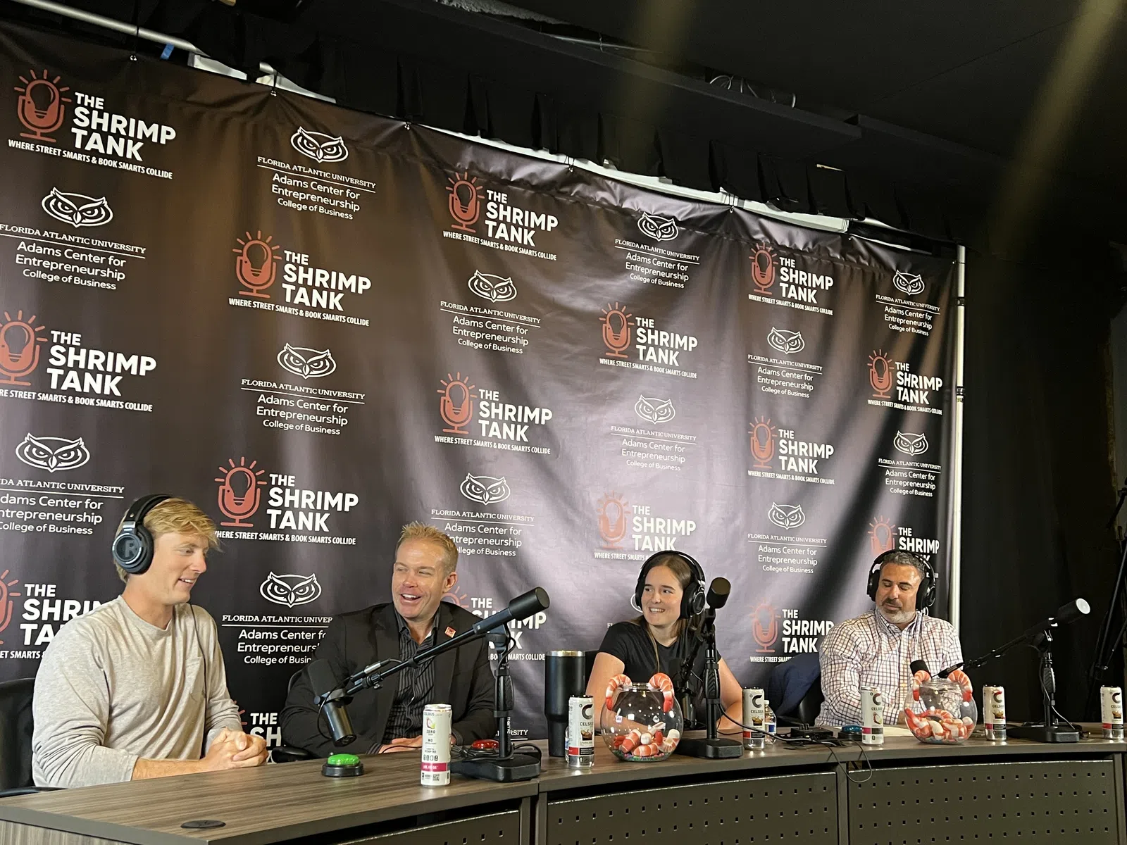 Four people wearing headphones talking into microphones at a Shrimp Tank podcast panel event