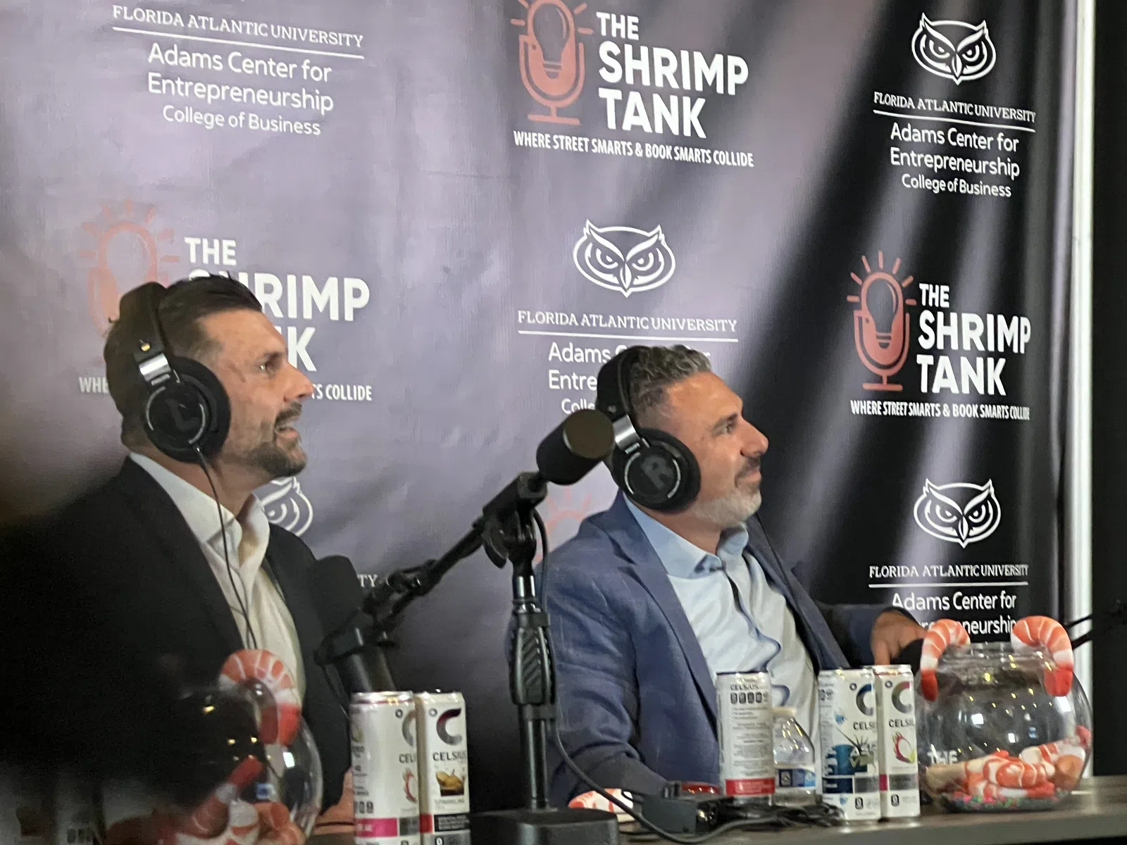 Two men in suits wearing headphones speaking into microphones during The Shrimp Tank podcast at Florida Atlantic University.