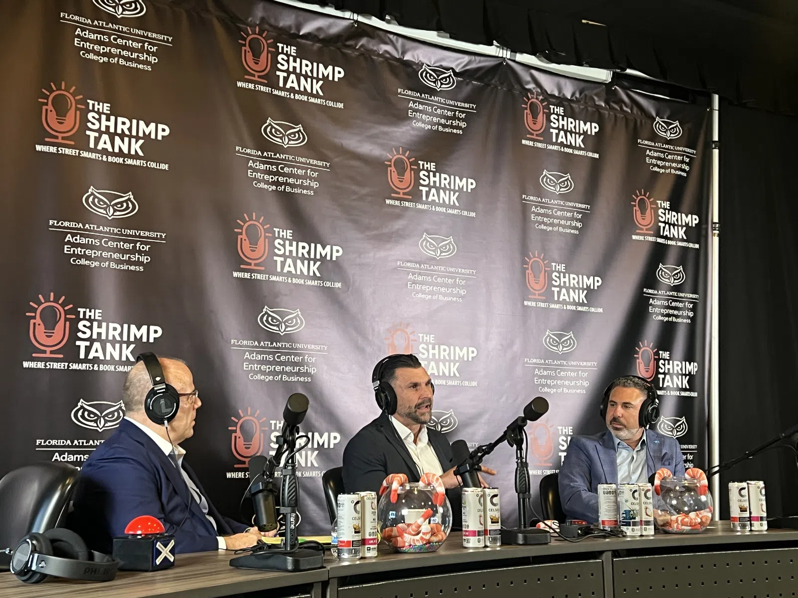 Three men wearing headsets talk into microphones during a Shrimp Tank podcast recording with branded backdrop.