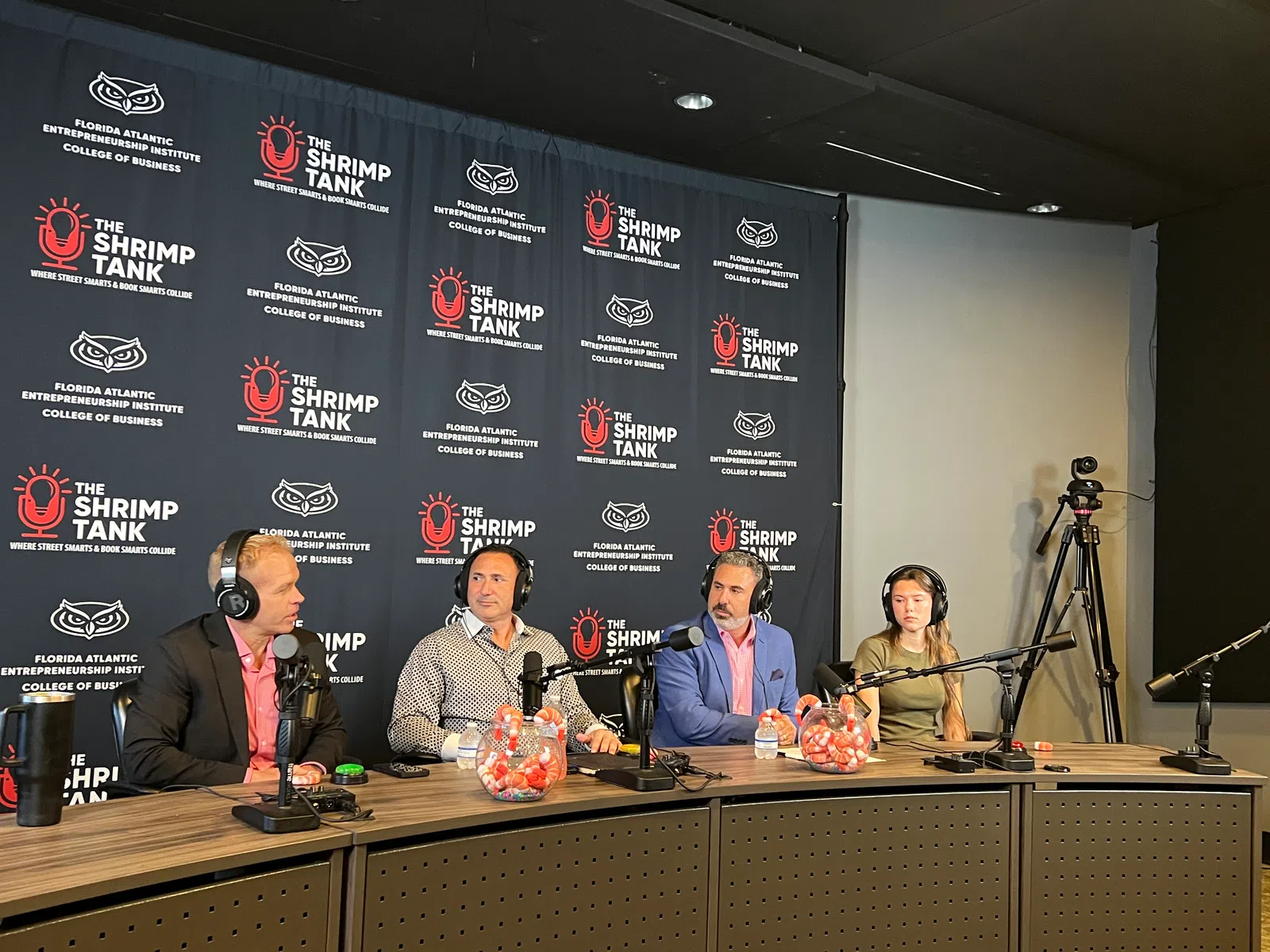 Panel of four podcasters with microphones on a set branded with The Shrimp Tank and Florida Atlantic Entrepreneurship Institute logos