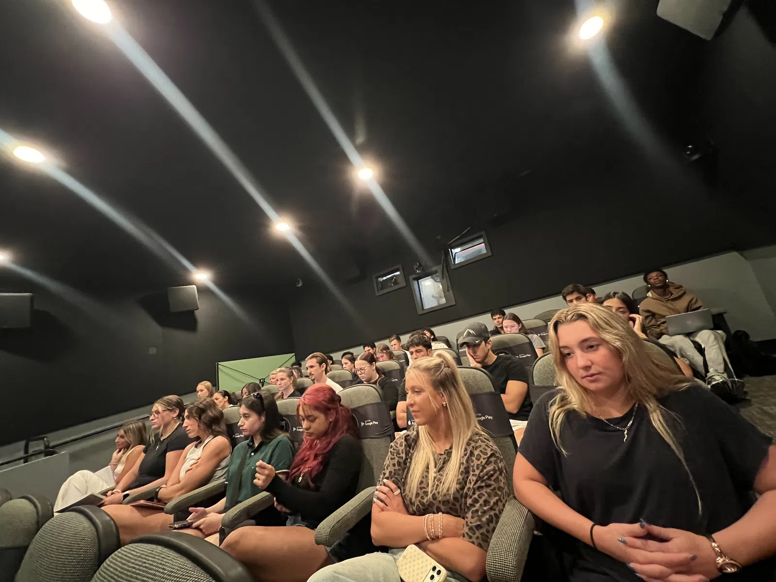 Diverse group of people attentively watching a presentation or film in a dark auditorium with tiered seating.