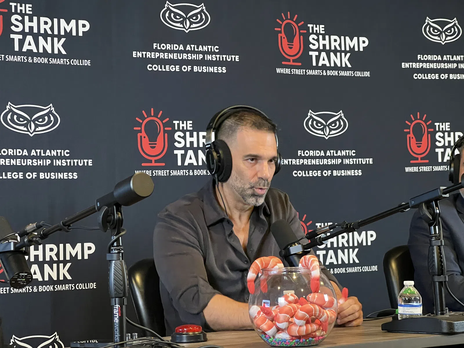 Man with headphones speaking into microphone at The Shrimp Tank event with branded backdrop and shrimp bowl