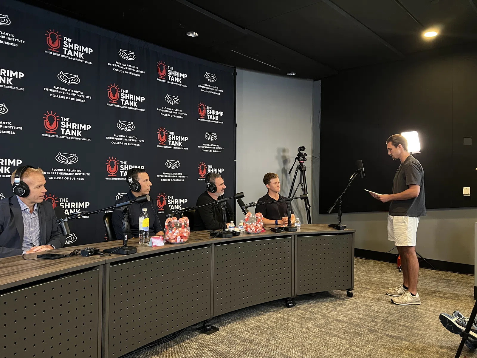 Panel of four men with headsets at a conference table in a recording studio for The Shrimp Tank show.