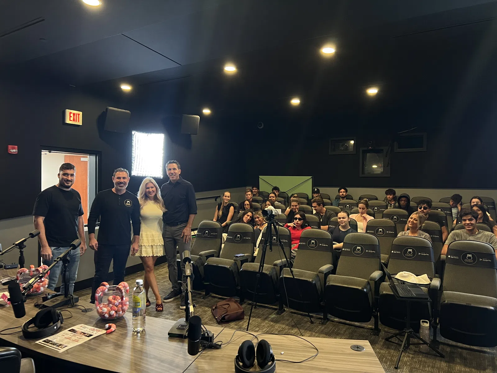 Group photo of speakers and audience in a small theater-style room with microphones and recording equipment.