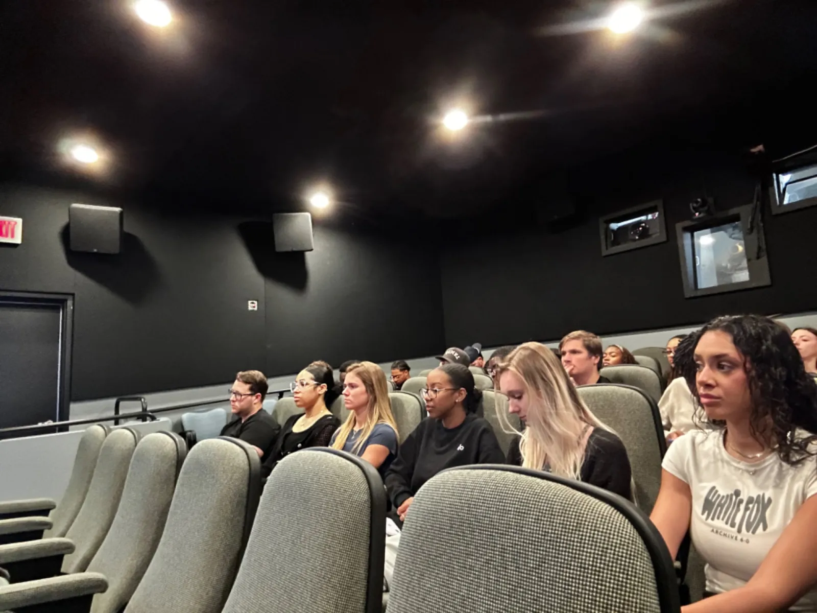 A group of people attentively watching a presentation in a small, modern theater setting.