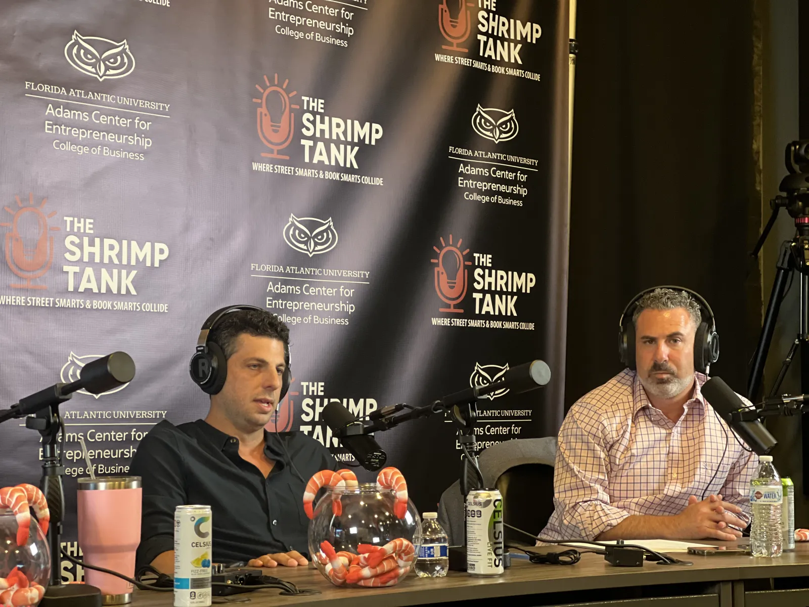Two men wearing headphones speaking into microphones on a podcast with The Shrimp Tank banner background