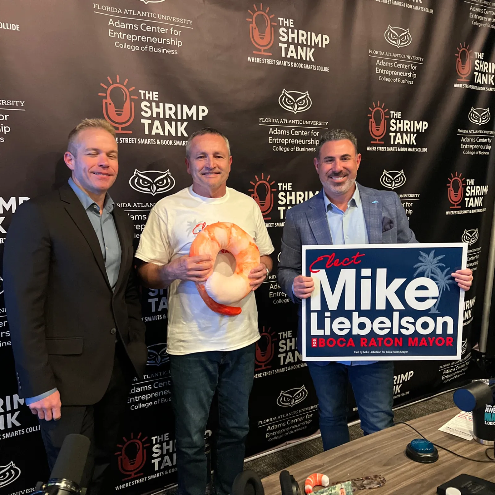 Three men at The Shrimp Tank event with campaign sign and shrimp prop, promoting Mike Liebenson for Boca Raton mayor.