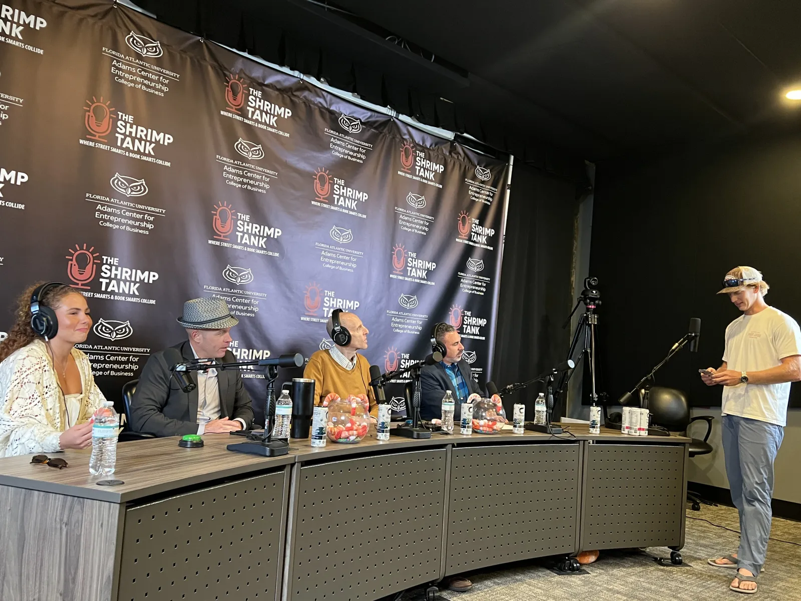 Panel of four podcast hosts with microphones and headphones in a studio branded The Shrimp Tank