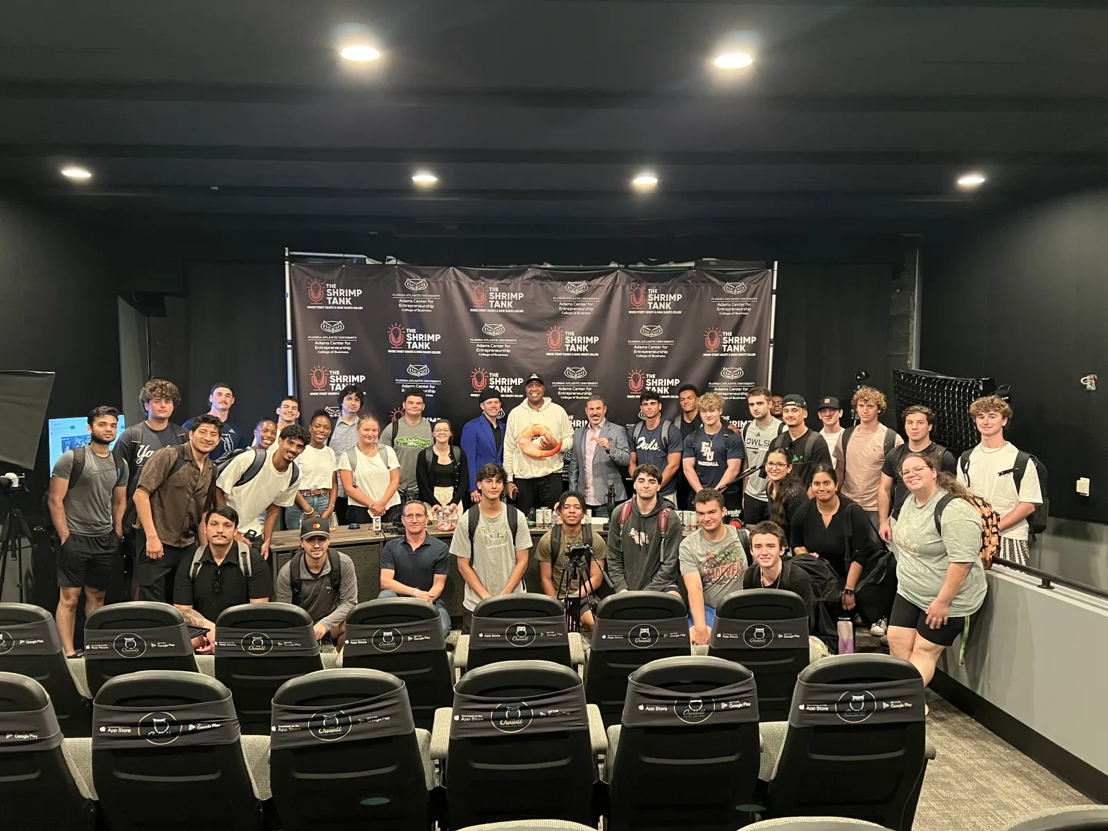 Group photo of diverse young adults in a seminar room with Shrimp Tank branding backdrop and seats in front