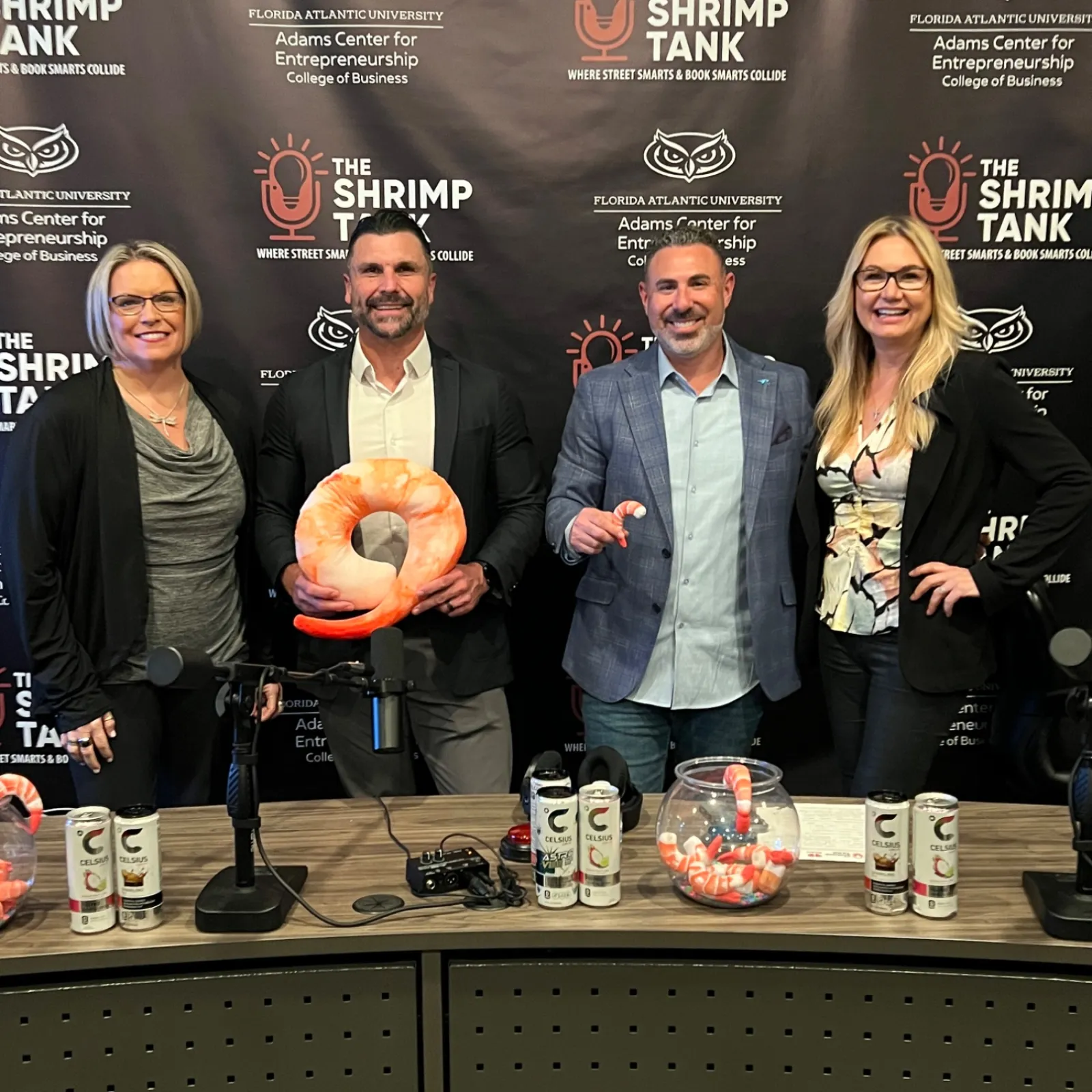 Four people smiling at a podcast table with shrimp-themed decorations and The Shrimp Tank backdrop