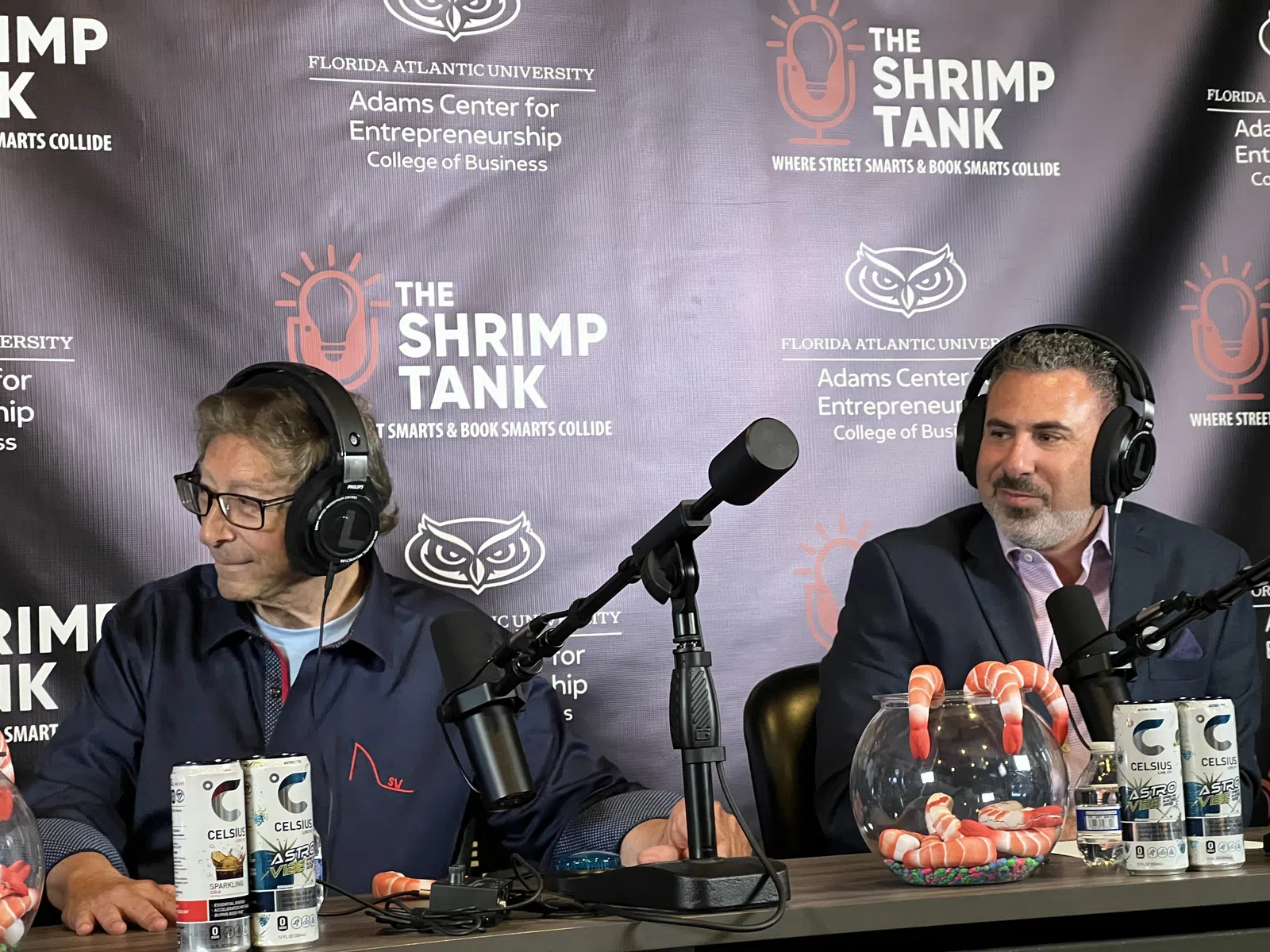 Two men with headphones sitting at a podcast table with microphones and Celsius energy drinks during The Shrimp Tank event.