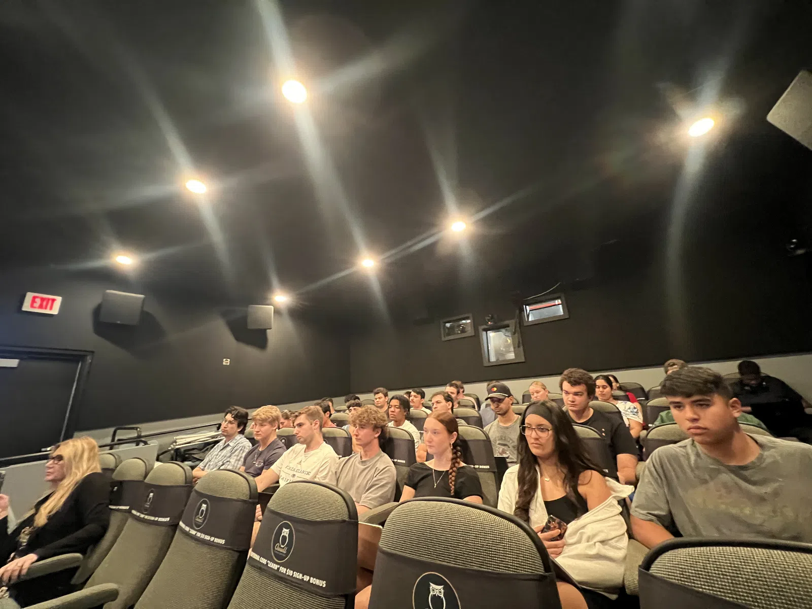 Group of young adults seated in a dark auditorium or classroom, attending an event or lecture.