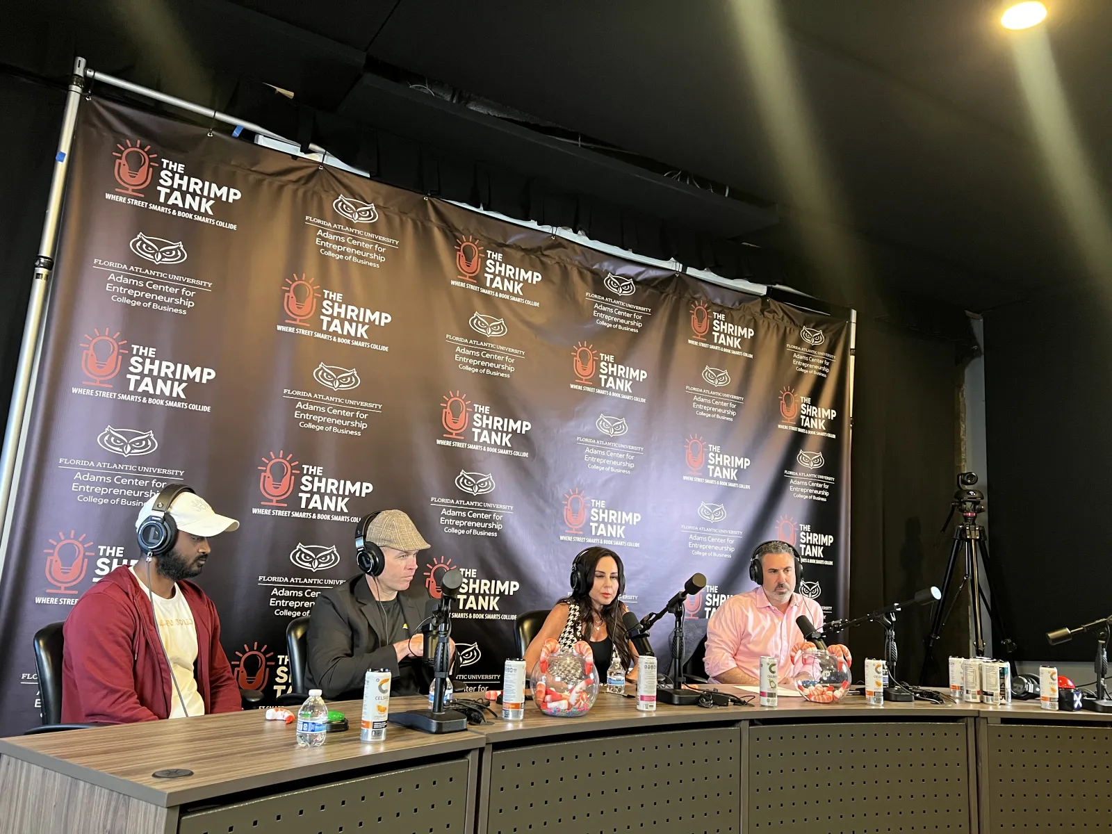 Panel of four hosts and guests with microphones at The Shrimp Tank event table with branded backdrop