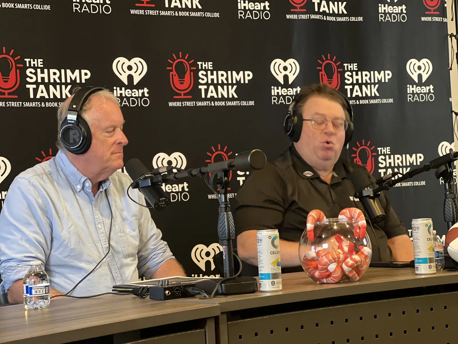 a couple of men sitting at a table with microphones and a basket of popcorn