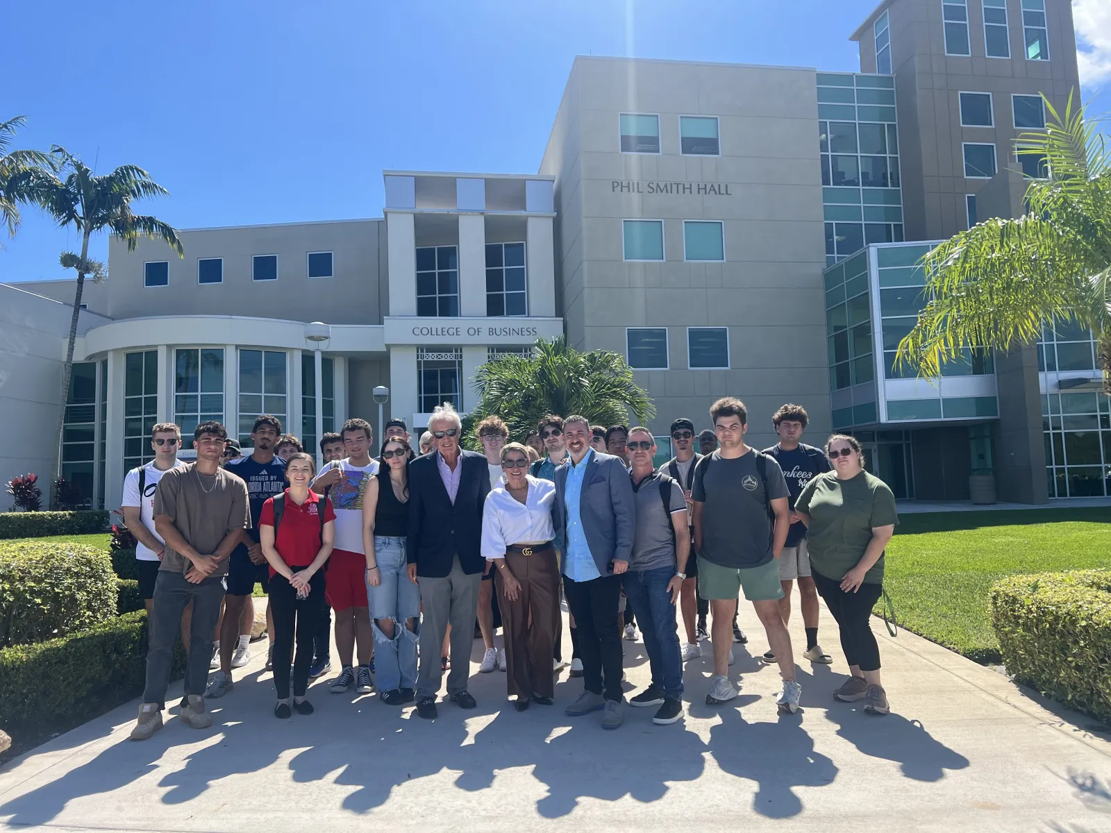 Group of students and faculty standing outside Phil Smith Hall at the College of Business on a sunny day.