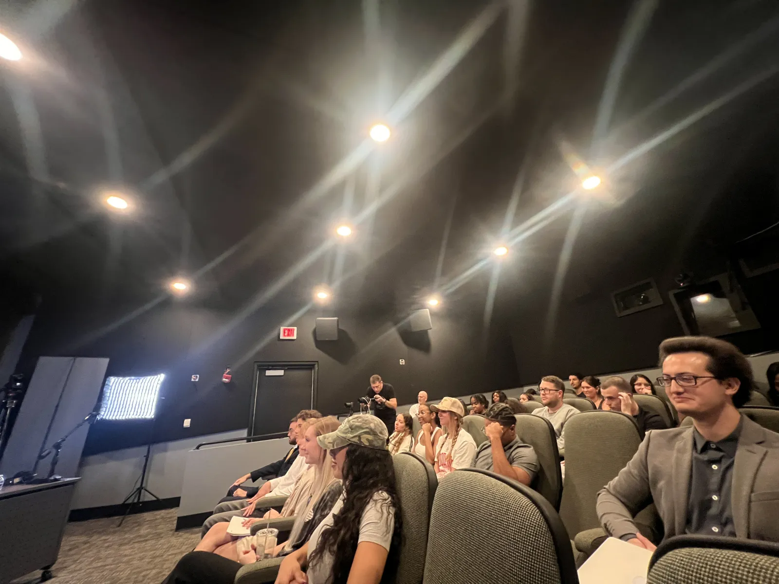 a group of people sitting in a room with a large screen