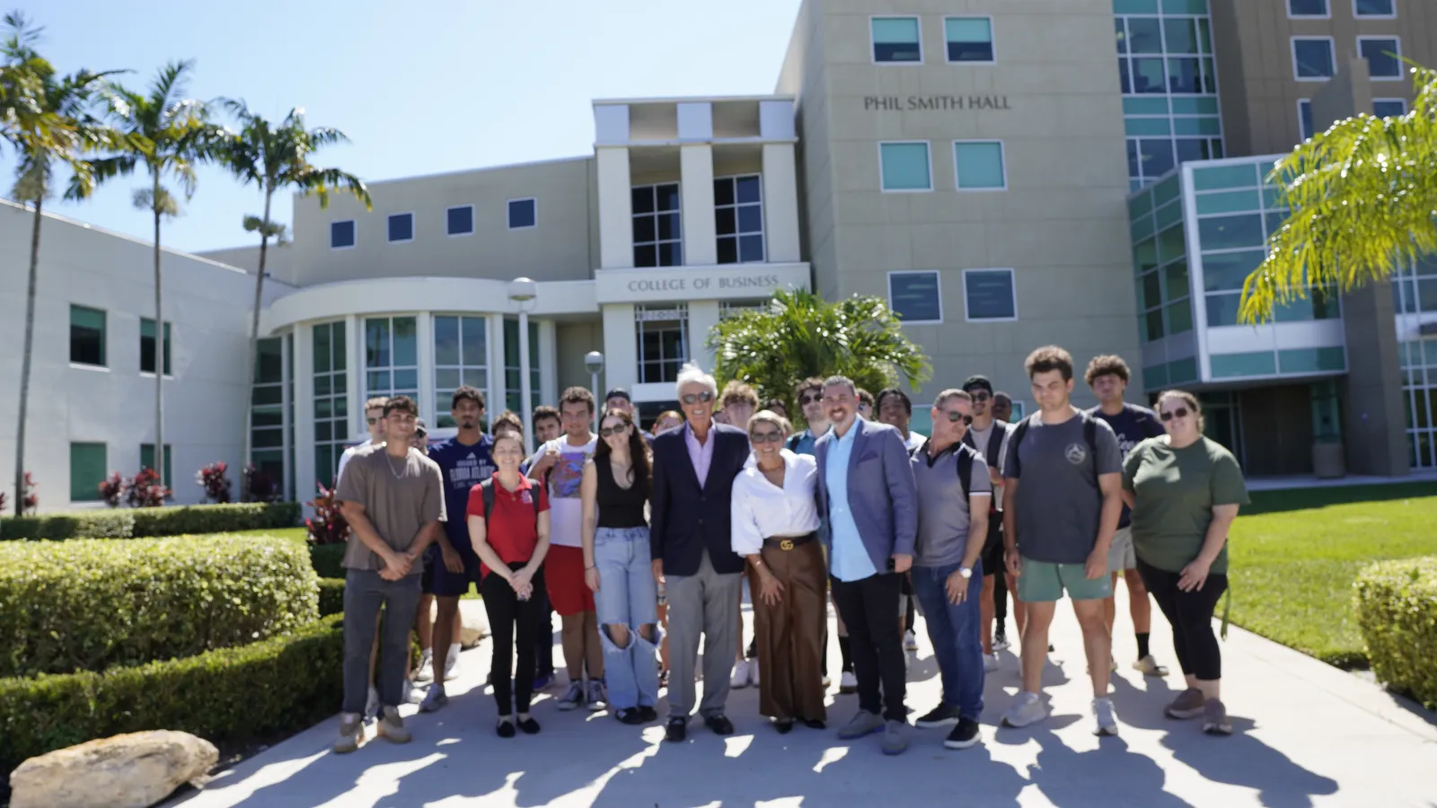 Group of diverse students and faculty posing outside Phil Smith Hall College of Business on a sunny day.