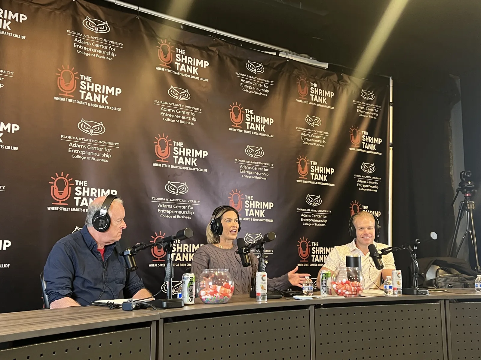 a group of people sitting at a table with microphones and a blackboard behind them