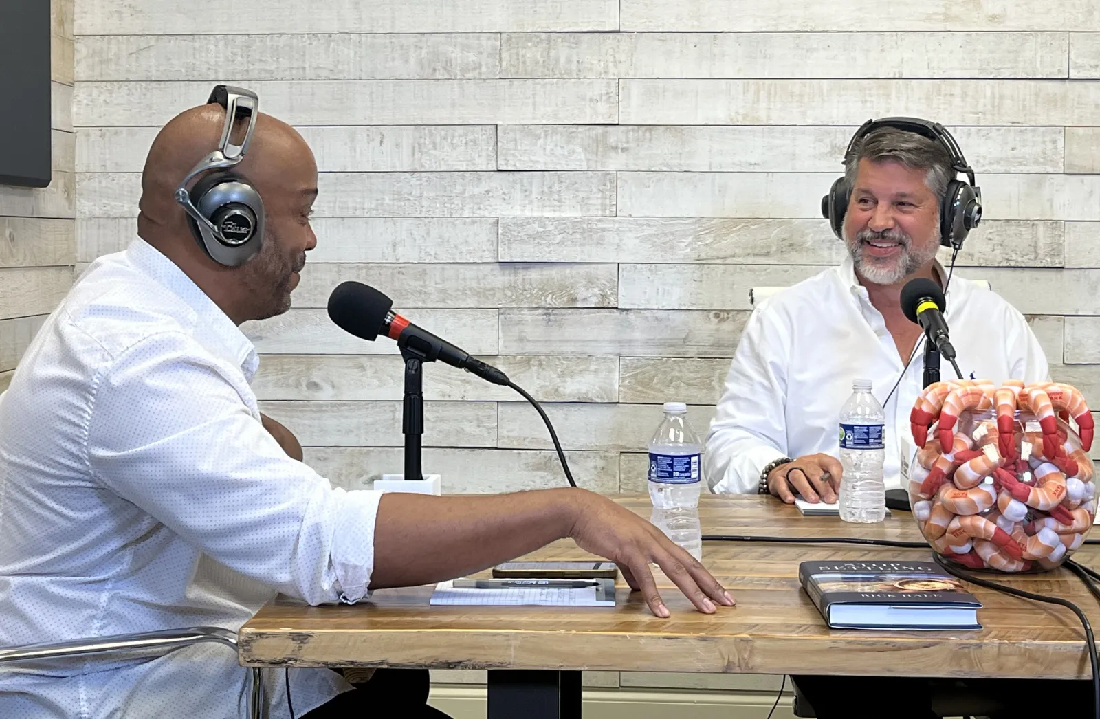 a couple of men wearing headphones and sitting at a table with a microphone