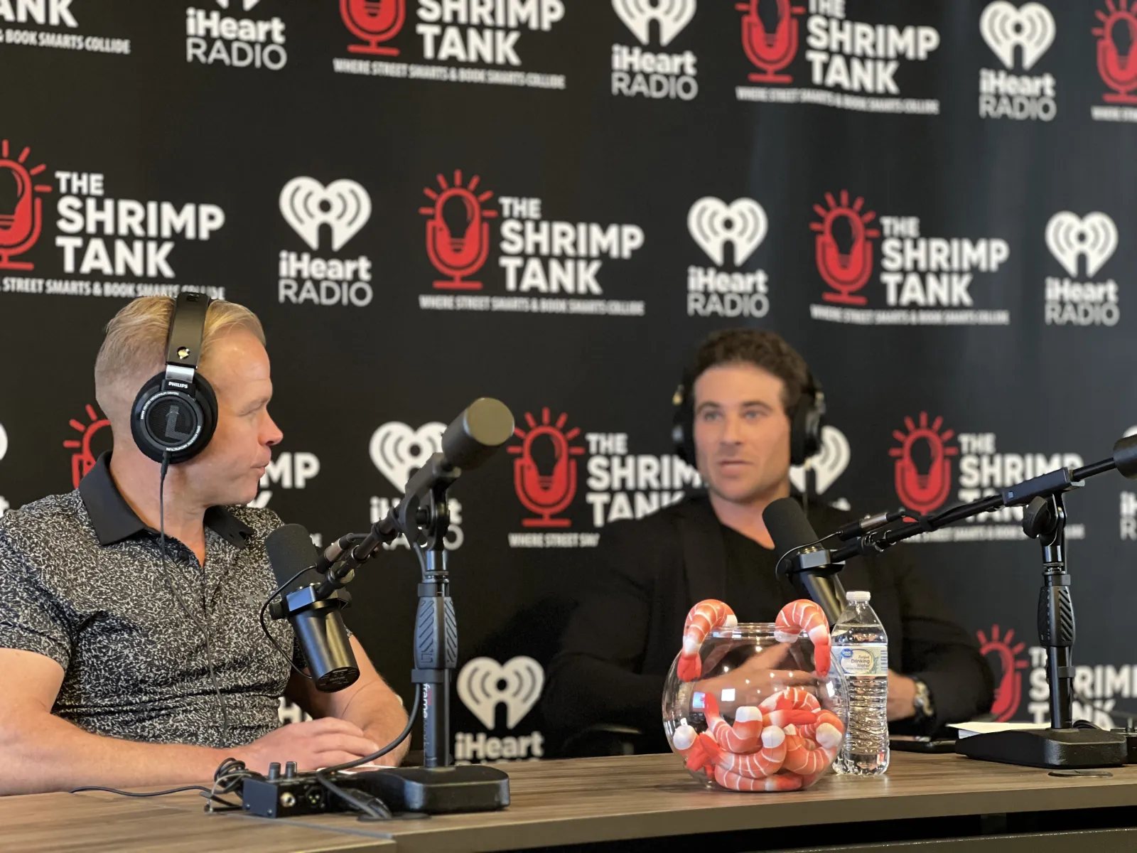 a couple of men wearing headphones and sitting at a table with microphones