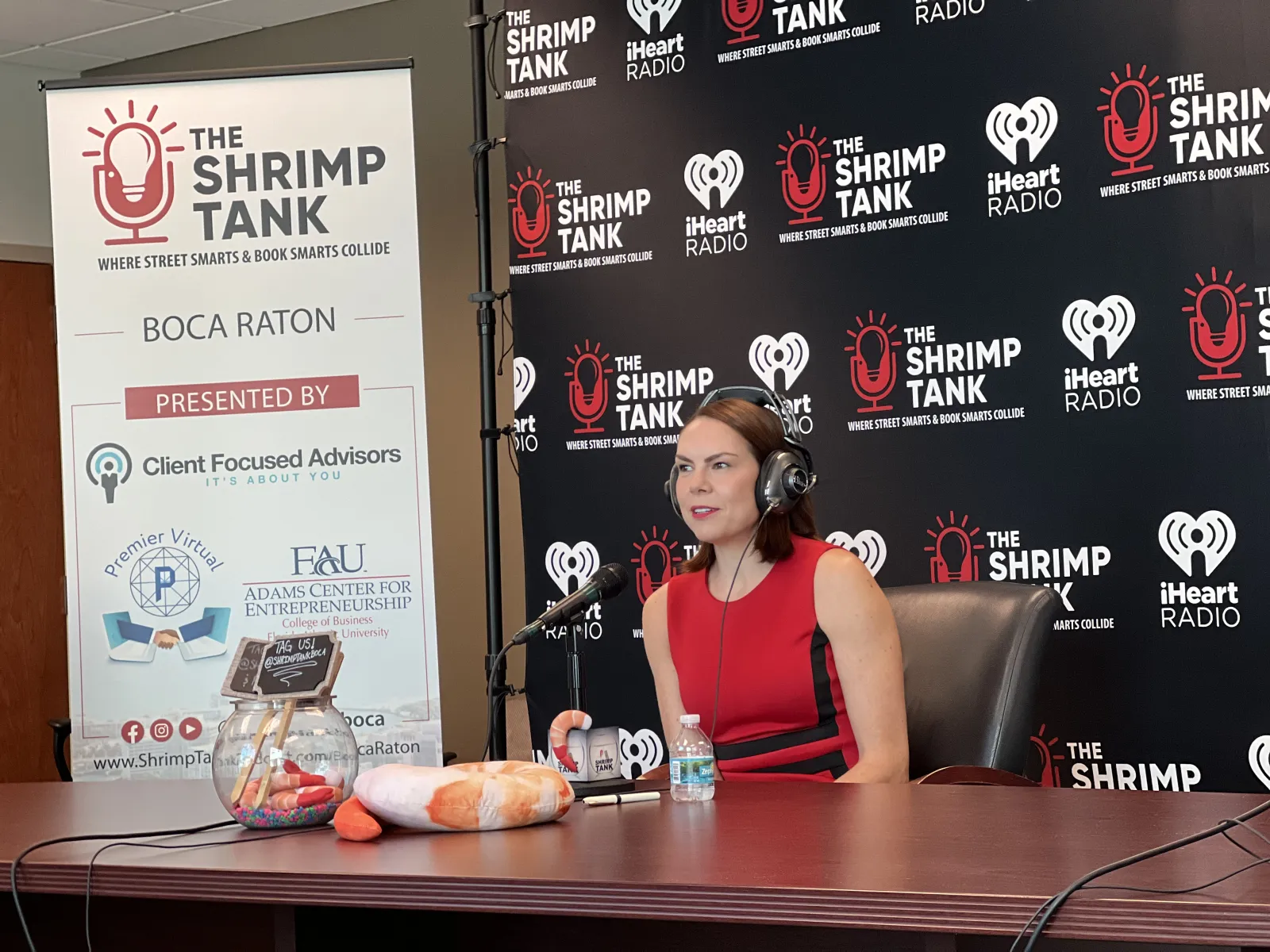 a person sitting at a table with a microphone and a sign behind the