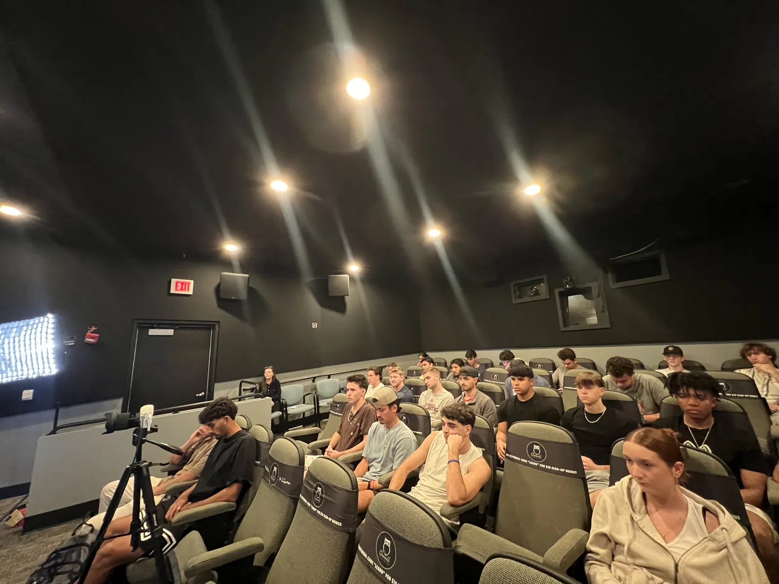 Group of young adults seated in a dark room with cinema-style chairs and bright filming lights