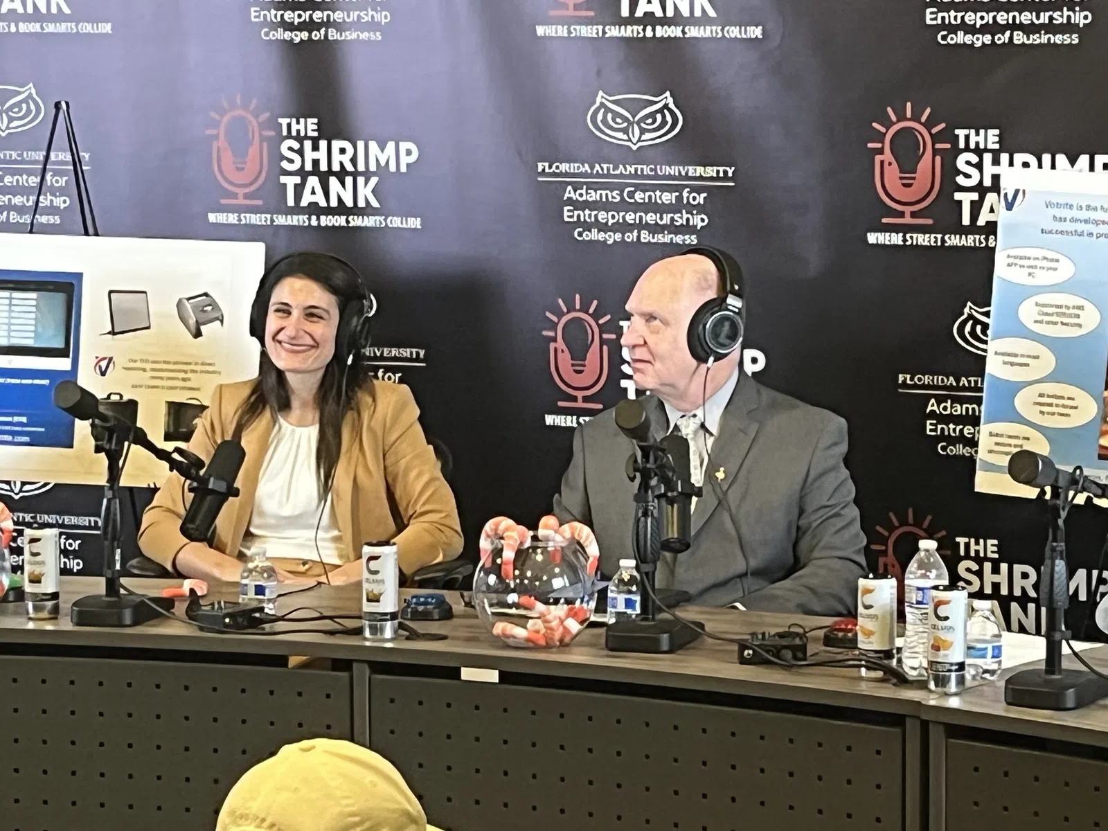 Two people with headphones speak into microphones hosting The Shrimp Tank podcast at Florida Atlantic University event