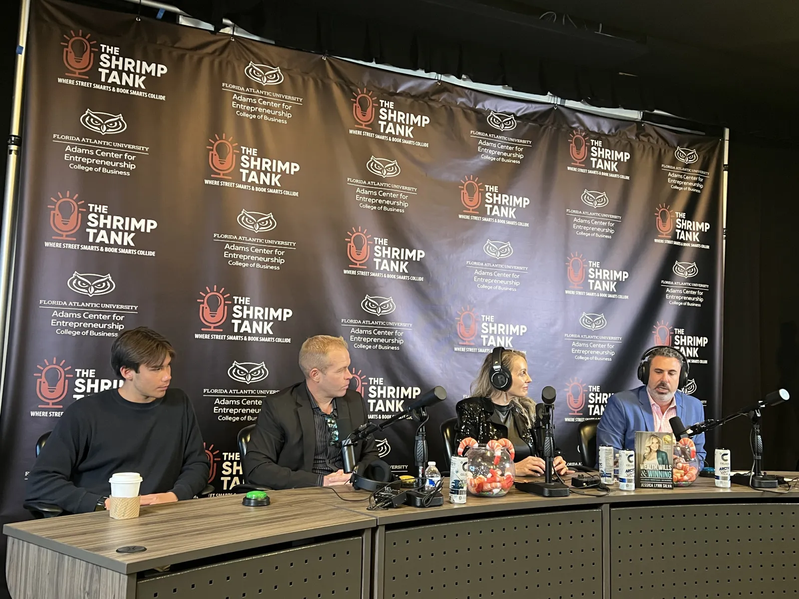 Four people seated at a table with microphones, recording a podcast or panel discussion at The Shrimp Tank event.