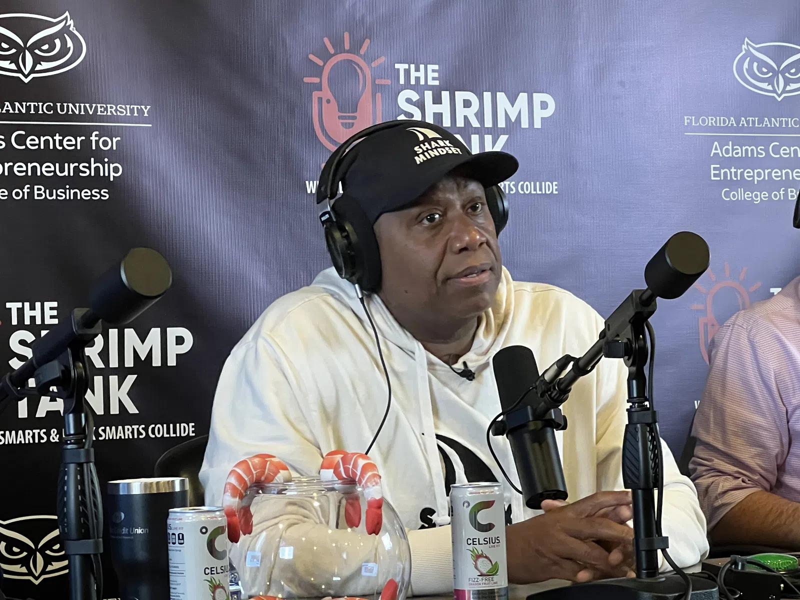 Man wearing headphones and a Shark Mindset cap speaking into a microphone at The Shrimp Tank podcast setup