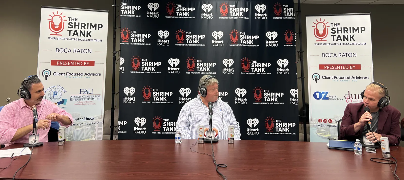 a couple of men sitting at a table with microphones and a sign