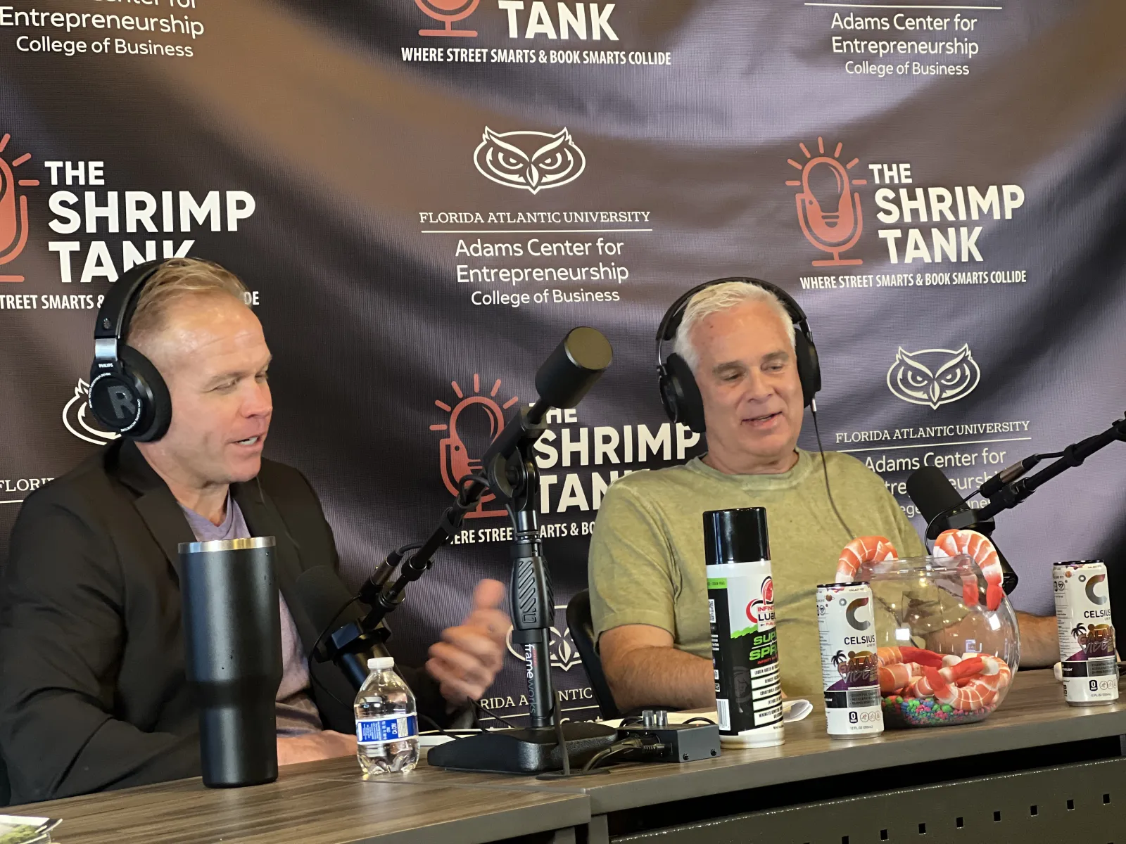 a couple of men sitting at a table with microphones and drinks