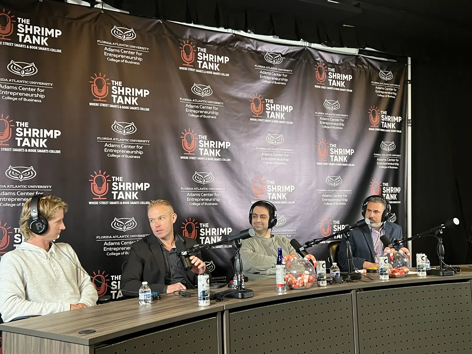 Four men with microphones and headphones sitting at a panel table during The Shrimp Tank event at Florida Atlantic University.
